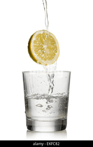 L'eau s'écoule plus de citron et remplir un verre sur fond blanc Banque D'Images