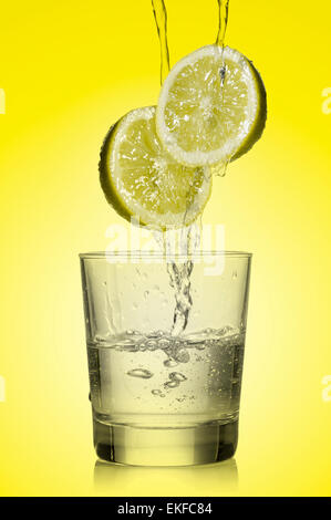L'eau s'écoule plus de citron et remplir un verre sur fond jaune Banque D'Images