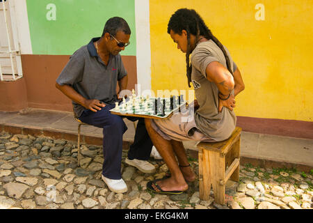 Cuba Trinidad pavées de galets de rue deux hommes jouer aux échecs sur la toile de fortune à bord perché sur les genoux Banque D'Images