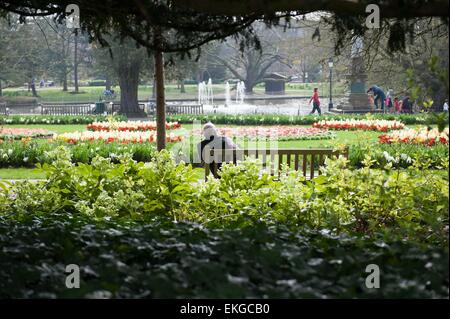 Un homme âgé est assis seul sur un banc de parc en face de certaines fontaines dans un lac. Banque D'Images