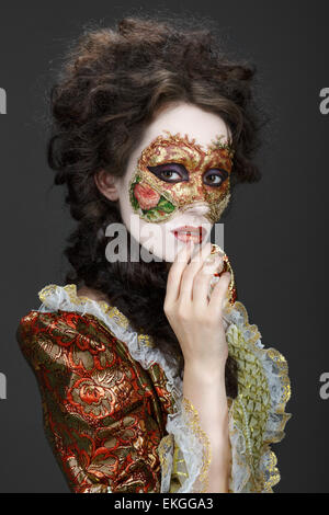 Faceart. Masque de Venise. Belle femme en robe d'époque et un masque sur son visage. D'œil timide à l'appareil photo. Banque D'Images