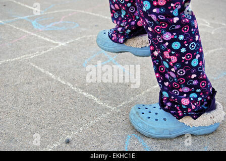 Jeune fille jouant à la marelle sur le trottoir de ciment. Banque D'Images