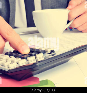 Libre d'un jeune homme avec une tasse de café dans sa main contrôle de comptes avec une calculatrice au bureau Banque D'Images