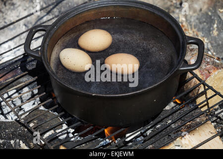 Oeufs dans un chaudron en fonte pleine de l'eau bouillante sur un feu de Camping Banque D'Images