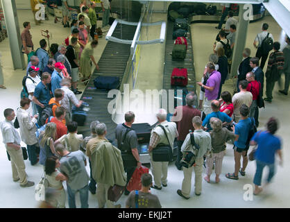 Les gens à l'aéroport en attente de leurs bagages à la courroie de transport des bagages Banque D'Images