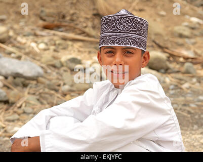 Un garçon vêtu d'un kummah omanais traditionnels (cap) se détend dans un wadi ci-dessous date de son grand-père plantation. Banque D'Images