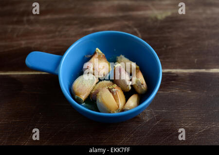 De l'ail grillé saupoudré de sel de mer en bleu pot en céramique sur table en bois brun Banque D'Images