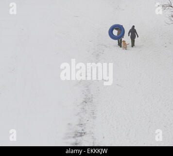 Deux personnes avec un chien suivant derrière une grande chambre à air jusqu'a snowy winter hill avant de descendre en luge Banque D'Images