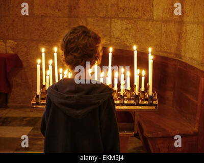 Un jeune garçon à la recherche de quelques bougies allumées dans une église Banque D'Images