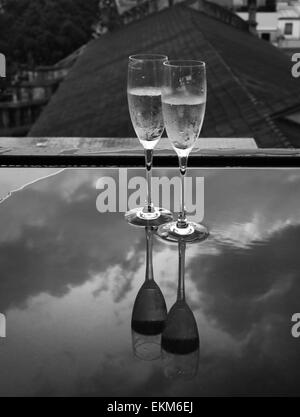 Verres de champagne sur une table sous la pluie avec des réflexions Banque D'Images