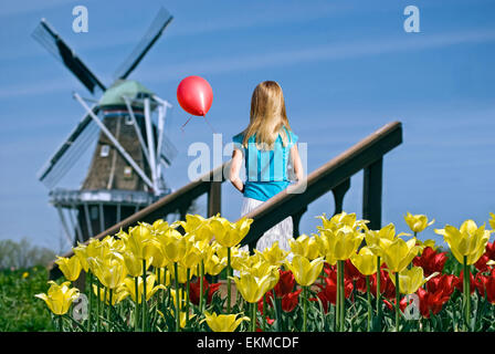 Jeune fille avec ballon rouge dans un jardin hollandais avec moulin à vent. Banque D'Images