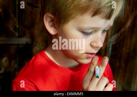 Portrait d'enfant garçon blond cigarette avec fond en bois sombre derrière lui Banque D'Images