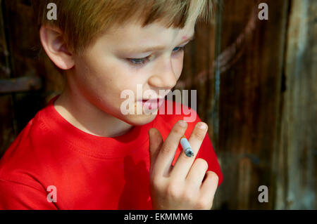 Portrait d'enfant garçon blond cigarette avec fond en bois sombre derrière lui Banque D'Images