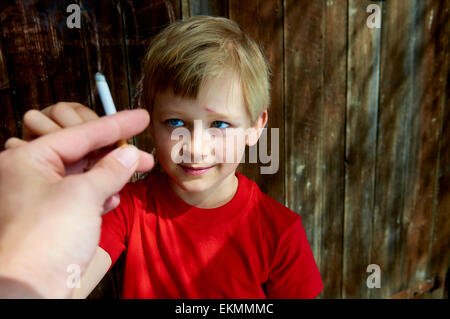 Portrait d'enfant garçon blond cigarette avec fond en bois sombre derrière lui. Hot man main offrant une cigarette pour garçon Banque D'Images