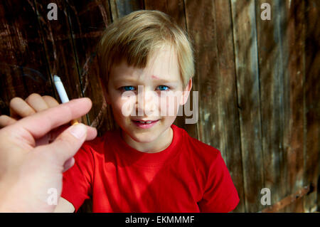 Portrait d'enfant garçon blond cigarette avec fond en bois sombre derrière lui. Hot man main offrant une cigarette pour garçon Banque D'Images