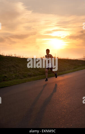 Adolescent triathele fonctionnant dans le cadre d'une course de duathlon avec coucher de soleil en arrière-plan à Gravesend Cycloparc PPJ d'avance Banque D'Images