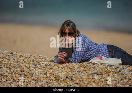 Une femme lit son e-reader Kindle au soleil sur une plage. Banque D'Images