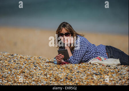 Une femme lit son e-reader Kindle au soleil sur une plage. Banque D'Images