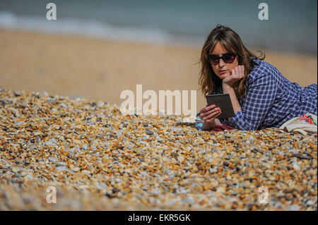 Une femme lit son e-reader Kindle au soleil sur une plage. Banque D'Images