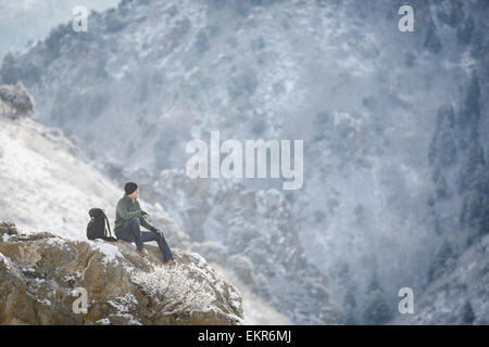 Un homme, un randonneur en montagne, prendre du repos sur un affleurement rocheux au-dessus d'une vallée. Banque D'Images