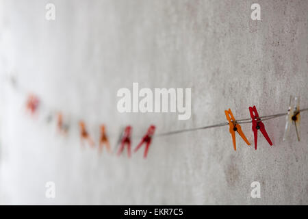 Des pinces à linge en plastique de couleur sur une ligne de lavage contre un mur blanc. Banque D'Images