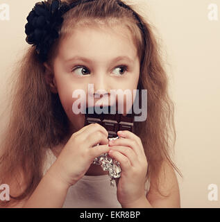 Happy kid girl eating chocolate surprenant et à cheveux longs avec style. Gros plan Vintage Banque D'Images