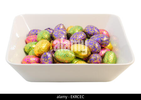 Oeufs de Pâques en chocolat de nombreux emballages colorés dans un bol, isolé sur fond blanc Banque D'Images