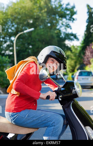 Femme âgée vive la trottinette habillés en vêtements à la mode et porter un casque de sécurité de rire comme elle chevauche par i Banque D'Images