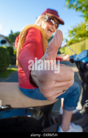 Happy senior woman giving Thumbs up, assis sur un scooter. Banque D'Images