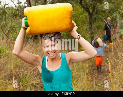 Une jeune femme porte une cruche d'eau sur sa tête ; Manica, Mozambique, Africa Banque D'Images