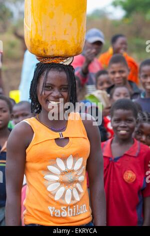 Une jeune femme équilibre une cruche d'eau sur sa tête ; Manica, Mozambique, Africa Banque D'Images