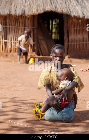 Une fille est titulaire d'un jeune enfant, assis sur le sol ; Manica, Mozambique, Africa Banque D'Images