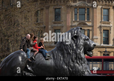 Famille touristiques siéger sur l'un d'un des quatre lions de Landseer conçu par à la base de la Colonne Nelson à Trafalgar Square. Banque D'Images