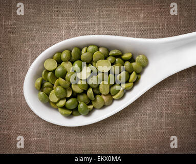 Pois cassés verts en cuillère en porcelaine blanche / haute résolution de grain dans cuillère en porcelaine blanche sur fond d'un sac de jute Banque D'Images