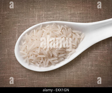 Le riz Basmati en cuillère en porcelaine blanche / haute résolution de grain dans cuillère en porcelaine blanche sur fond d'un sac de jute Banque D'Images
