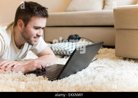 L'homme gisant sur le sol typing on laptop Banque D'Images