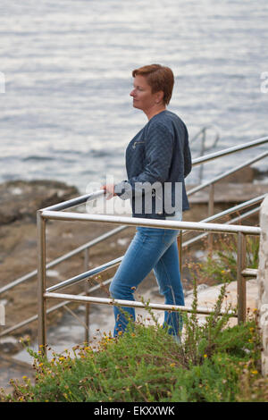 Middle aged woman femme bronzée en automne à la recherche de vêtements dans la mer pensivement Rocky beach Banque D'Images