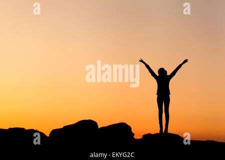 Silhouette of woman with arms raised up contre beau ciel coloré. Coucher du soleil d'été. Paysage Banque D'Images