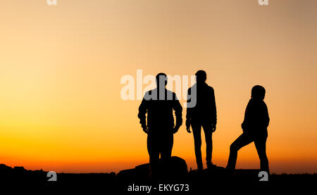 Silhouette d'une famille heureuse avec bras levés contre beau ciel coloré. Coucher du soleil d'été. Paysage Banque D'Images