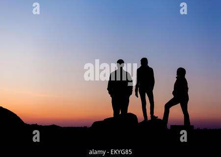 Silhouette d'une famille heureuse avec bras levés contre beau ciel coloré. Coucher du soleil d'été. Paysage Banque D'Images