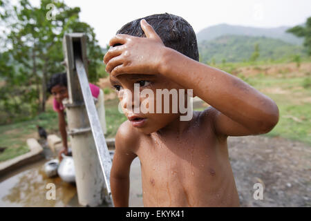 Un garçon se nettoie à l'eau froide au niveau du village ; pompe à eau Kharigoda Giajapati Village, District, Orissa, Inde Banque D'Images