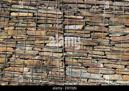 Mur avec pierres empilées derrière maille en acier Banque D'Images