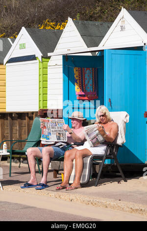 Bournemouth, Dorset, UK. 15 avril, 2015. Météo France : Les visiteurs de découvrir le beau temps chaud à la plage de Bournemouth, Dorset, UK privé prévoient que ce sera la journée la plus chaude de l'année au Royaume-Uni avec les températures dans le milieu des années 20 - couple à profiter du soleil de lire les journaux à l'extérieur beach hut Crédit : Carolyn Jenkins/Alamy Live News Banque D'Images