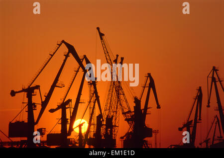 Silhouettes de grues portuaires contre ciel rouge. Scène industrielle. Banque D'Images