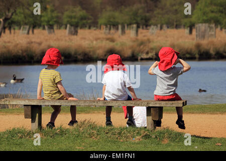 Bushy Park, SW London, England, UK. 15 avril 2015. Sur la journée la plus chaude de l'année jusqu'à présent, la température atteignait 25 degrés dans le sud ouest de Londres aujourd'hui. Ces enfants dans leurs bonnets rouges apprécié regarder les canards dans l'étang du héron Bushy Park. Credit : Julia Gavin UK/Alamy Live News Banque D'Images