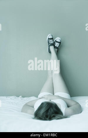 Femme allongée sur le dos sur un lit avec ses pieds sur le mur. Ses pieds sont croisés. Banque D'Images