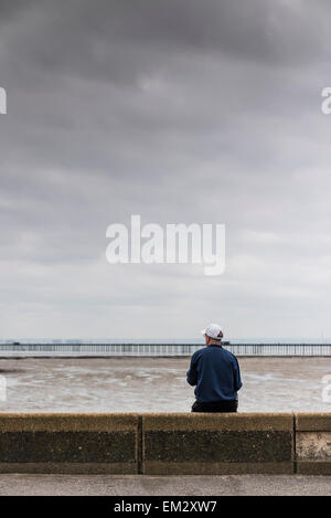 Un homme assis sur son propre front de Southend sur un jour nuageux. Banque D'Images