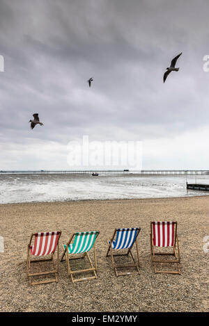 Vol de mouettes au-dessus des chaises vides sur la plage de Jubilee à Southend sur un jour nuageux. Banque D'Images