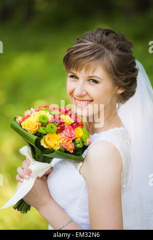 Jeune femme avec bouquet de fleurs dans ses mains l'article en vert parc d'été. Décor de mariage. Mariée avec mariage bouquet lumineux Banque D'Images