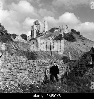 Château de Corfe Dorset s'élève derrière un mur de pierres sèches. Vieil homme sur l'épaule d'oignons d'équilibrage vers 1952 Banque D'Images